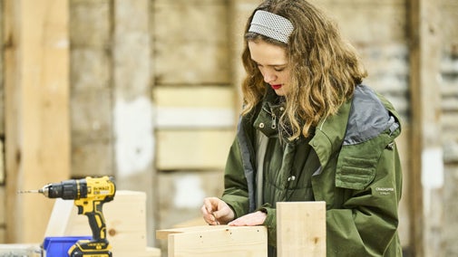 A young woman making a wooden birdfeeder in a workshop